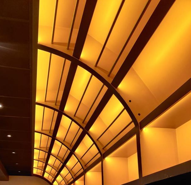 Gebogen plafond met amberkleurige indirecte verlichting tussen donkere spanten